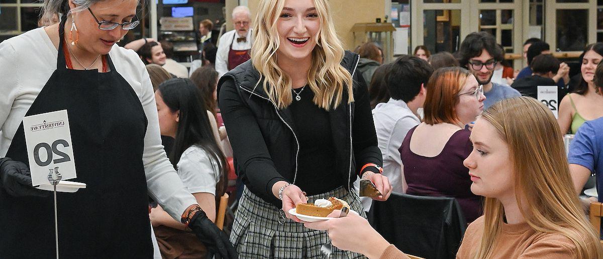 A student hands another a piece of pie.